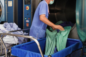 Laundry worker loading linens into a large industrial dryer machine.