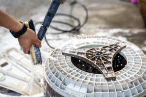 Worker cleaning a circular plastic component with a pressure washer in an industrial setting.