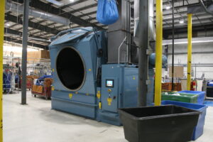 Hotel laundry facility with a large commercial dryer machine, ventilation ducts, and bins in a clean, organized production environment.
